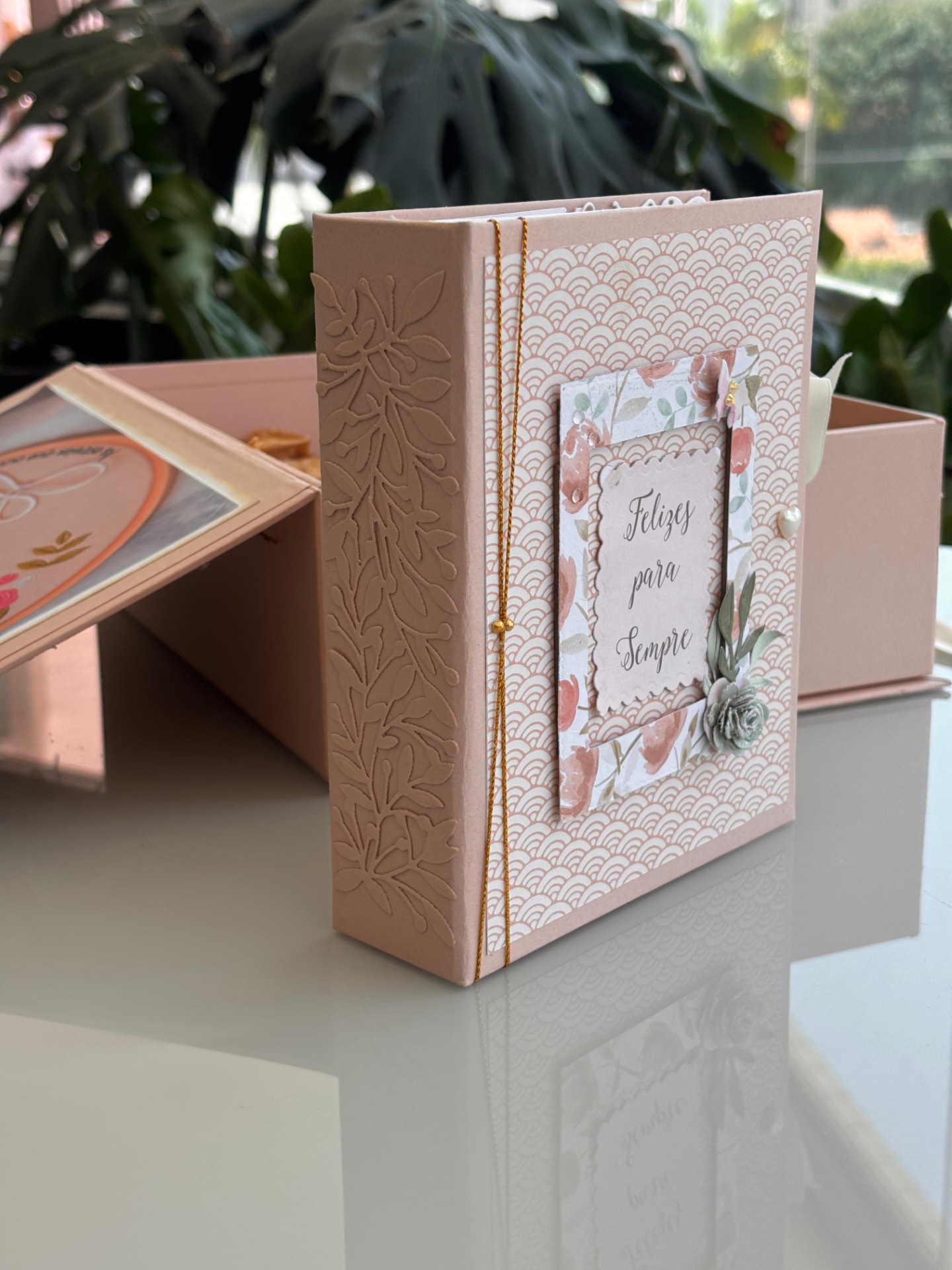 Álbum artesanal em tons de pêssego com a frase Felizes para Sempre na capa ao lado da caixa aberta