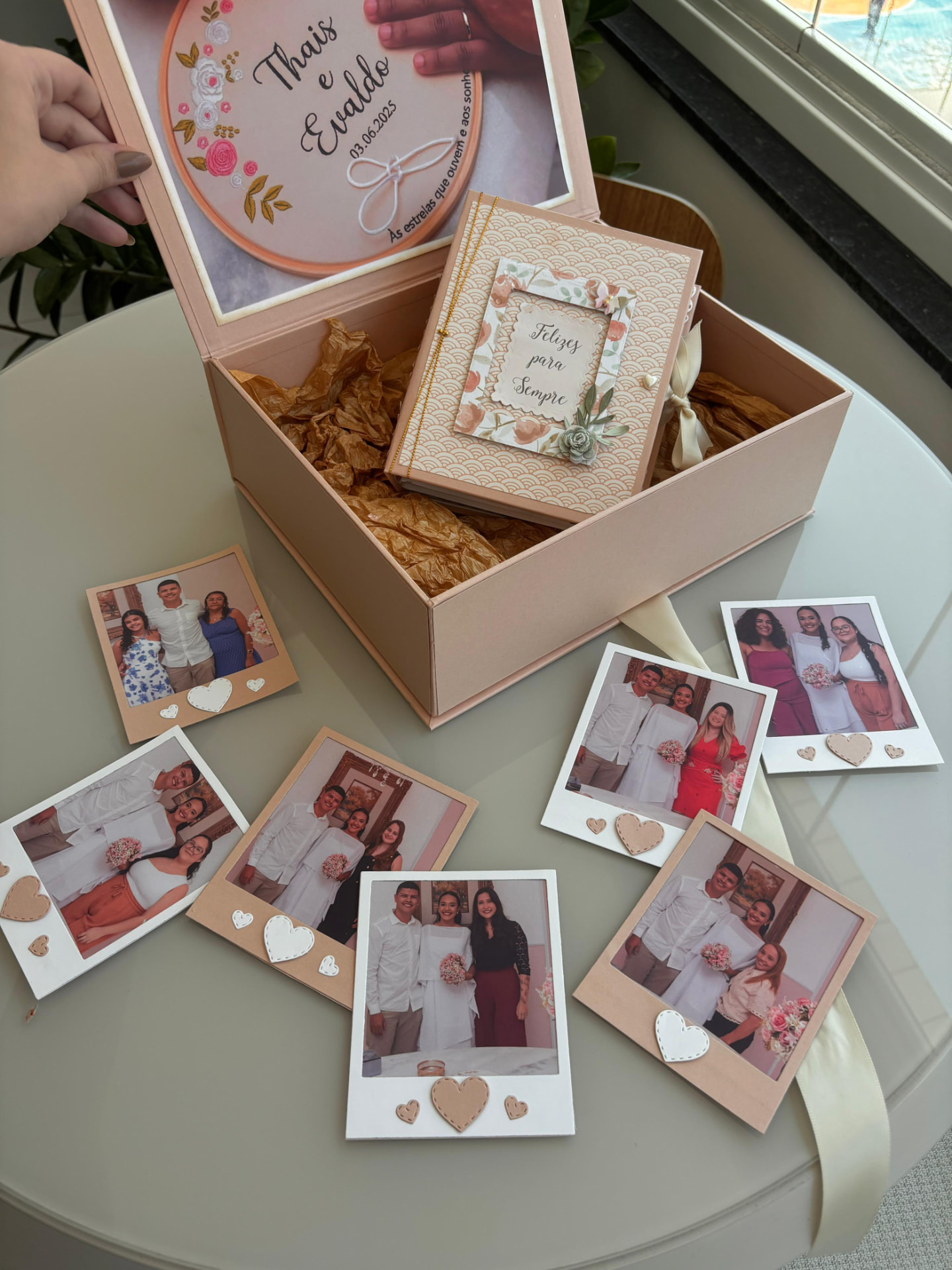 Caixa de presente de casamento aberta com bordado, um álbum e fotografias polaroid