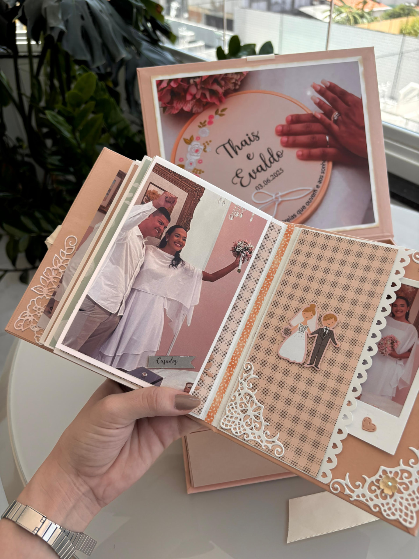 Álbum de recortes aberto exibindo fotos de casamento e elementos decorativos como rendas e adesivos