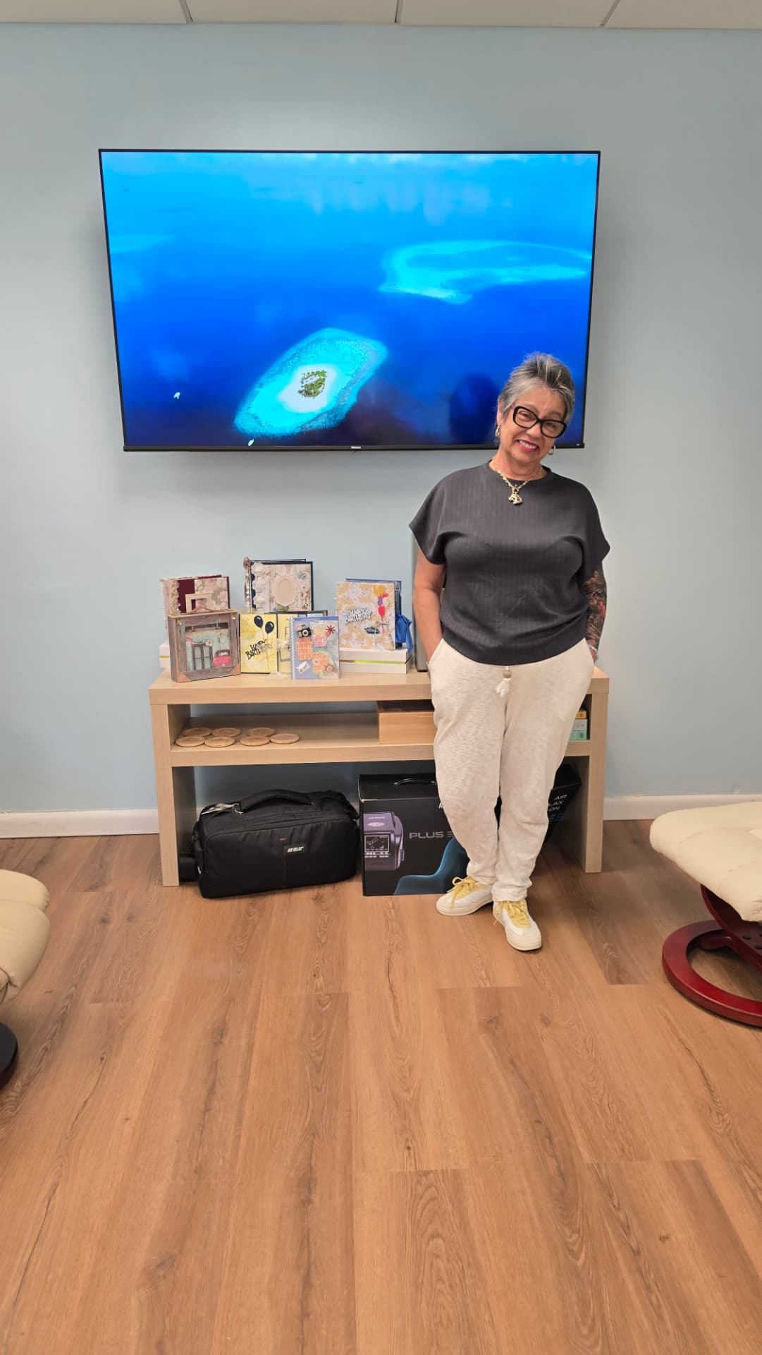 Mulher ao lado de mesa com vários álbuns de recortes, caixas de presente decoradas e decorações artesanais