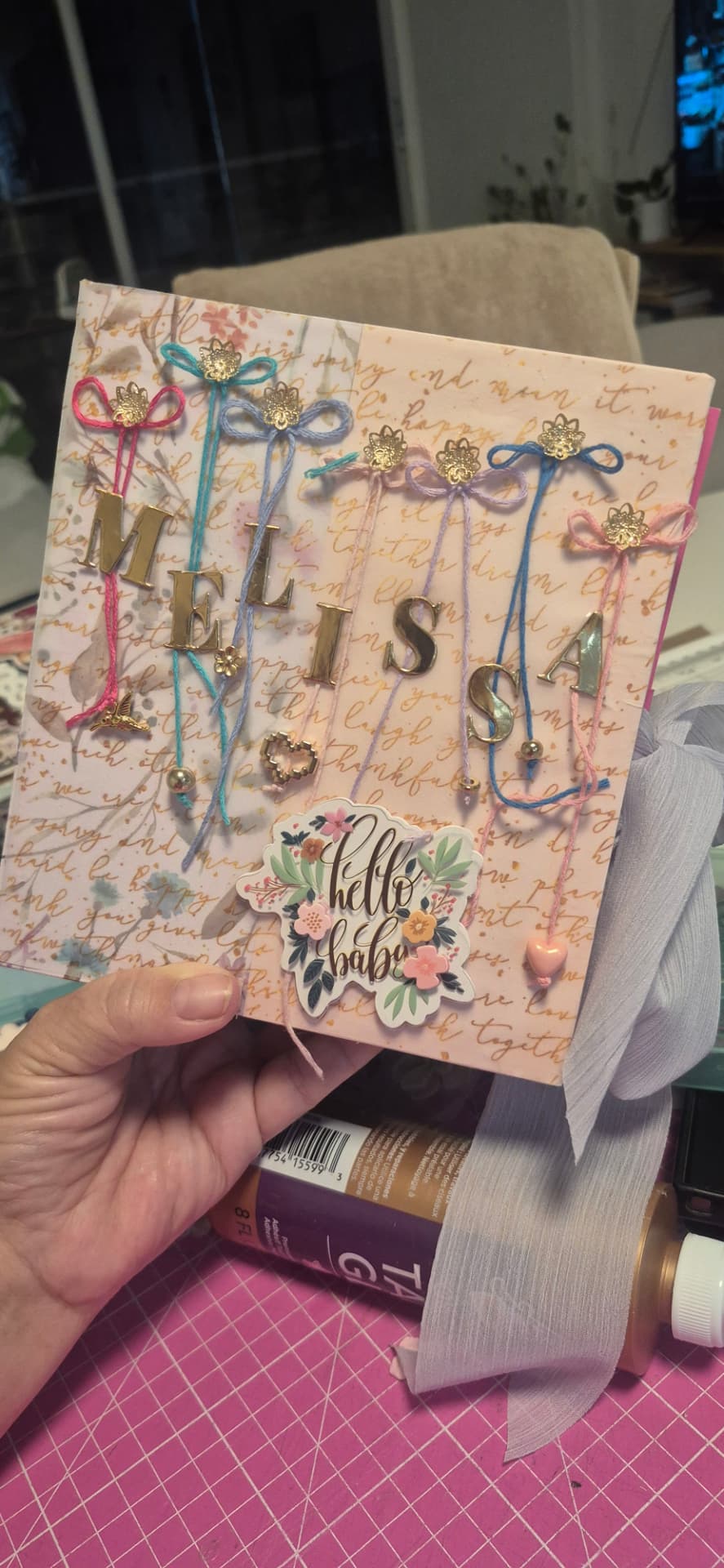 Capa de álbum rosa claro com o nome Melissa em letras metálicas douradas e adesivo Hello Baby